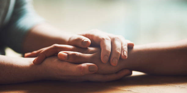 two people holding hands in comfort and prayer